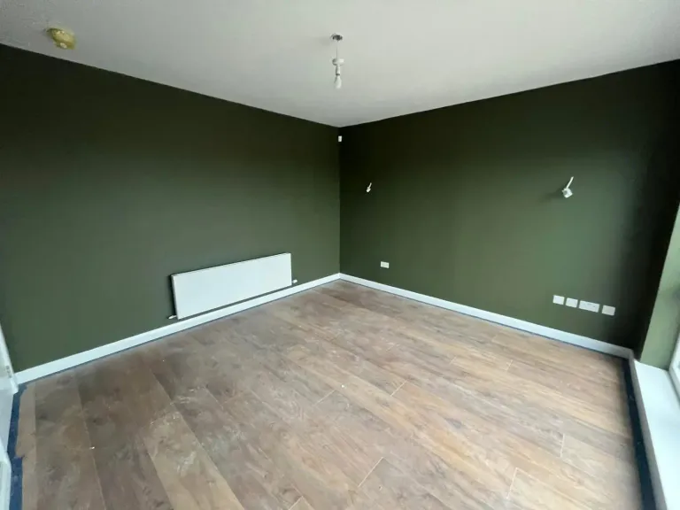 Bedroom with deep olive green walls and warm wood flooring