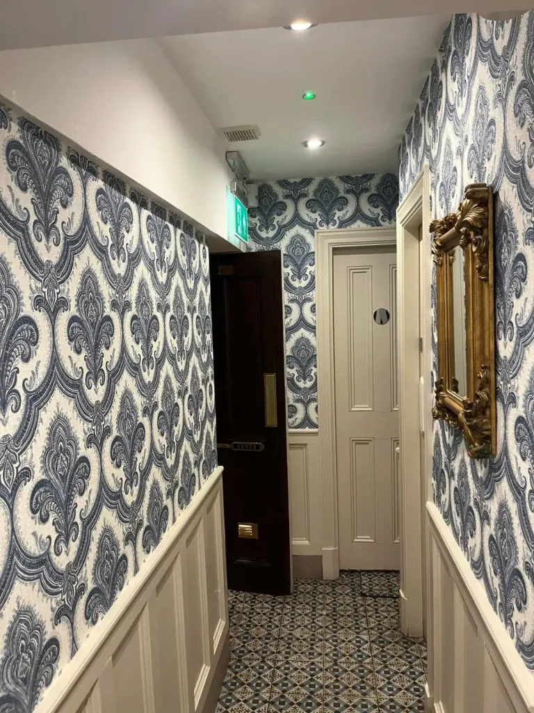 Hallway with blue damask wallpaper, white wainscoting and patterned tile floor