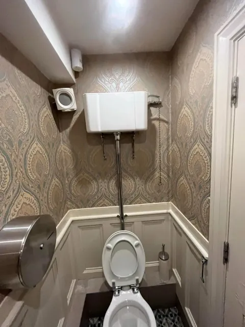 WC hung with beige damask wallpaper above white panelling