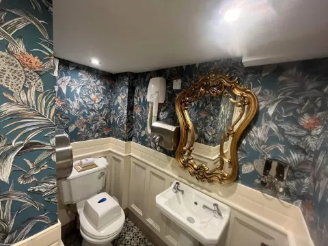 Cloakroom hung with blue jungle wallpaper and gold mirror
